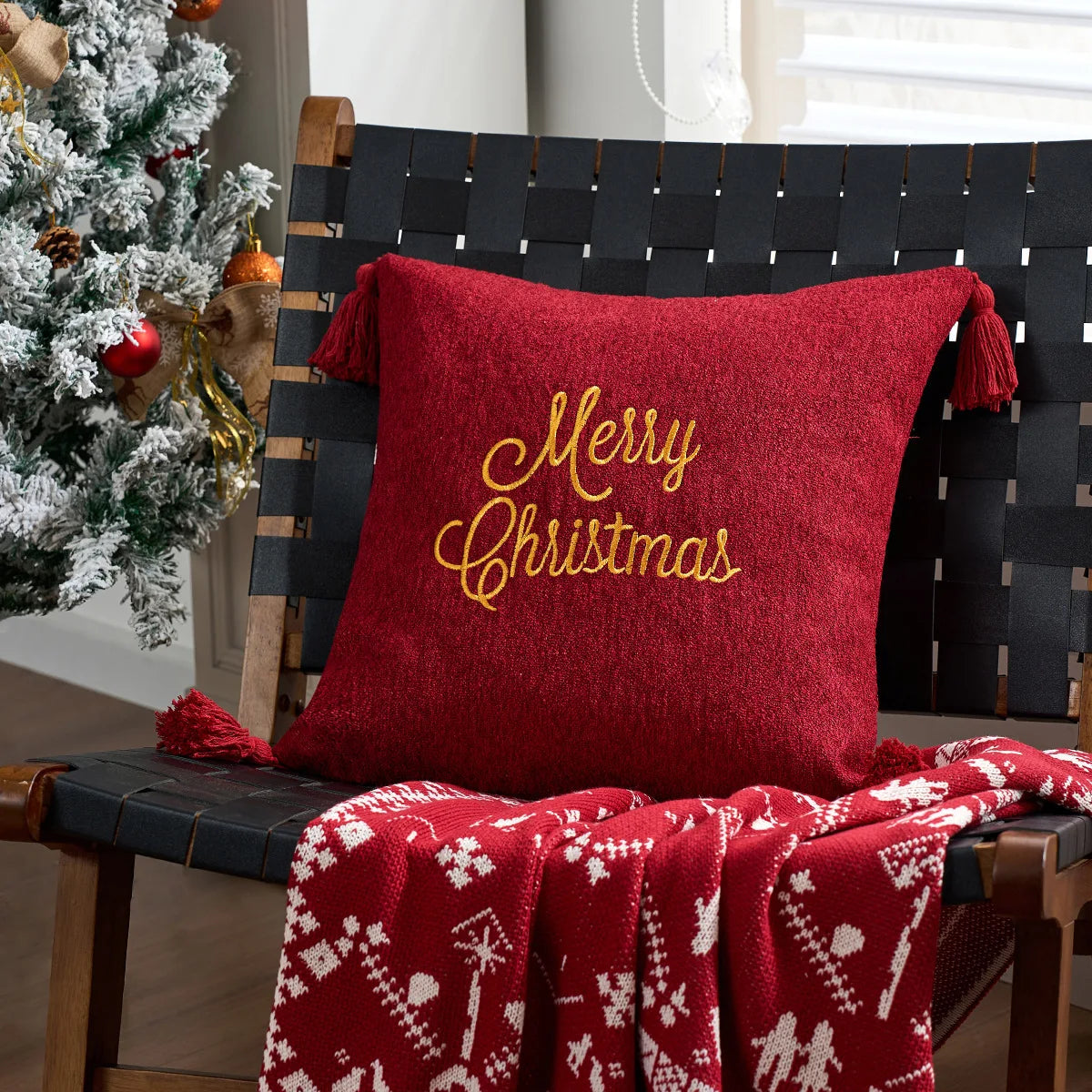 Red pillow with 'Merry Christmas' text on a black woven bench next to a decorated Christmas tree.