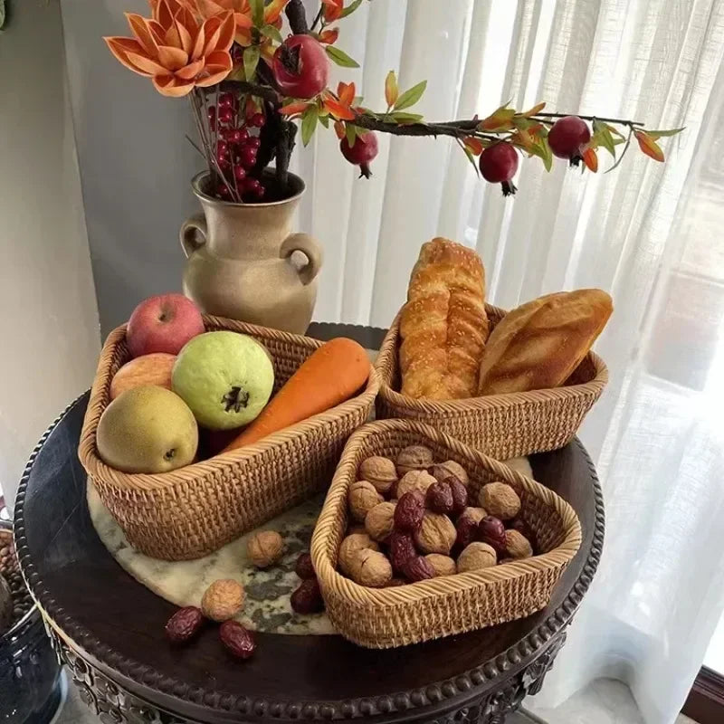 Three woven baskets on a table with fruits, bread, and nuts, with a vase of flowers in the background. boho home decor, rattan basket, handwoven wicker basket, fruit storage box, bread basket, picnic basket, natural storage bin, tea storage box, rustic home organization, farmhouse decor, housewarming gift, boho storage basket