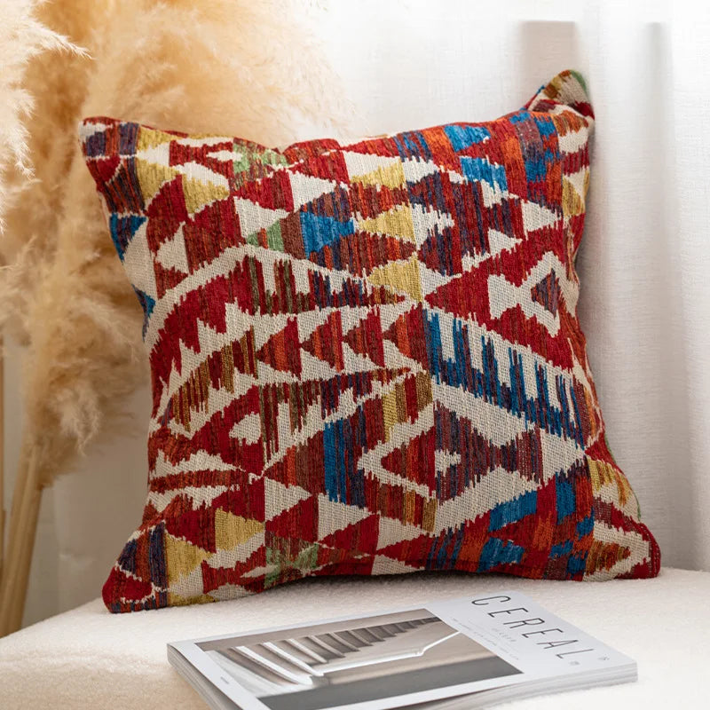 Multicolored patterned pillow on a white surface with a blurred background. Bohemian Aztec woven pillow cover, geometric jacquard cushion for sofa, bed, or living room decor in neutral cotton blend fabric.
