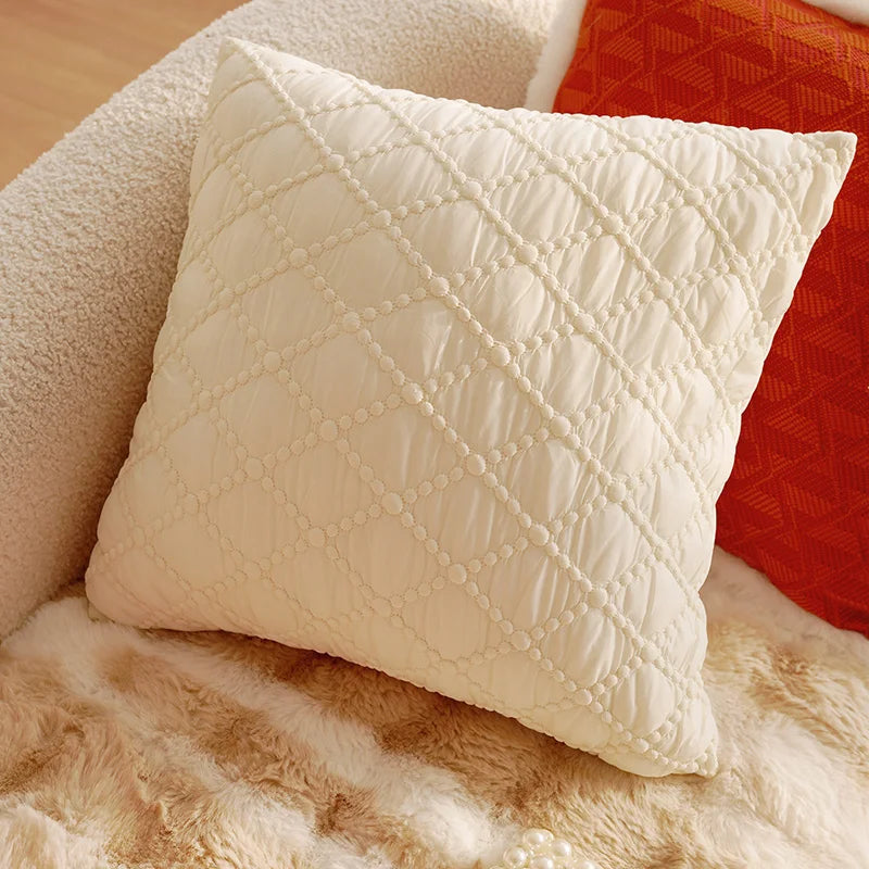 Quilted cream pillow on a textured surface with a red fabric background. Boho Home Decor.