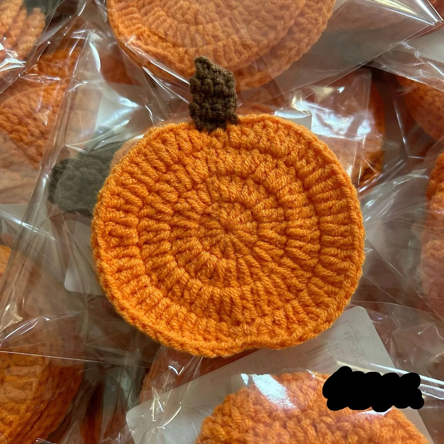 Crocheted orange pumpkin coasters with a brown stem on clear plastic packaging. Handmade crochet pumpkin coaster in cotton, Halloween table decor for mugs and drinks, festive DIY autumn party accessory.