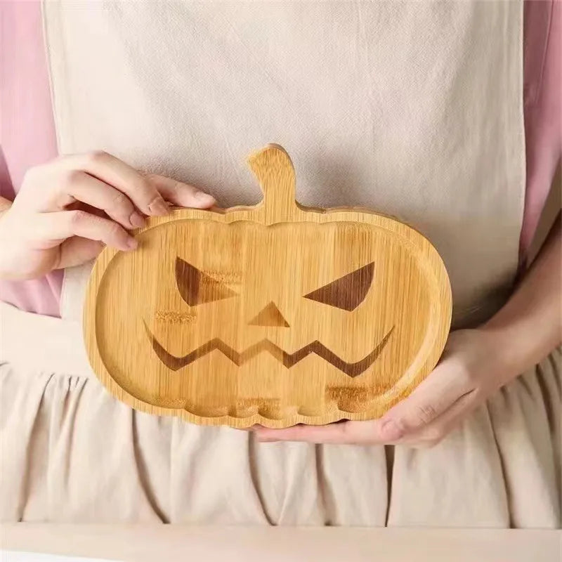 Person holding a wooden cutting board shaped like a pumpkin with a carved face. Wooden Halloween serving tray in pumpkin and ghost shapes, rustic snack and dessert plate for party décor and fall entertaining