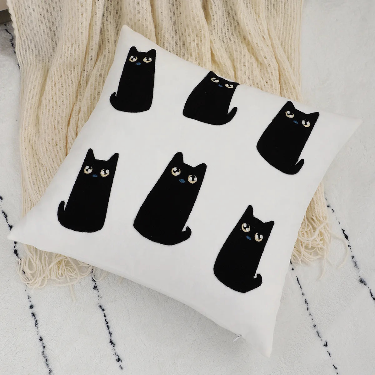 White pillow with black cat illustrations on a textured surface