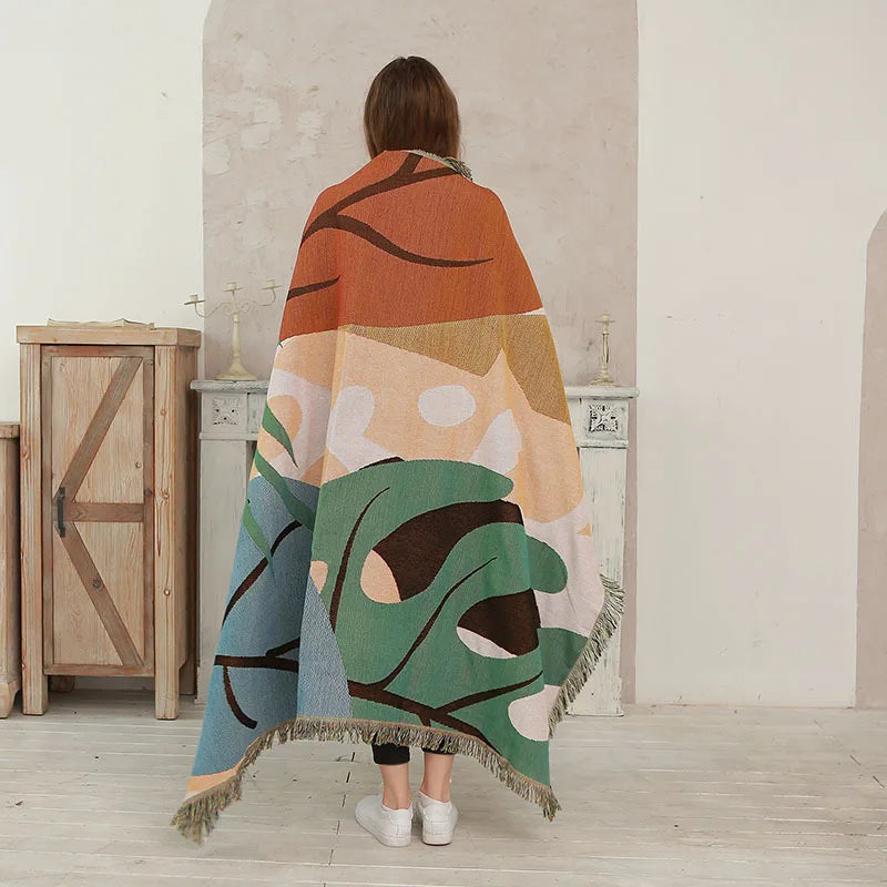 Person wrapped in a colorful abstract-patterned blanket in a minimalistic room. Boho Home Decor.