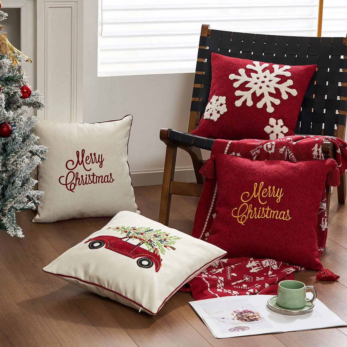 Decorative pillows with Christmas designs on a chair and floor next to a Christmas tree. Christmas gold letter embroidered pillow cover with “Holly Jolly” and snowflake design, soft red and white chenille cushion case for sofa or living room holiday décor.