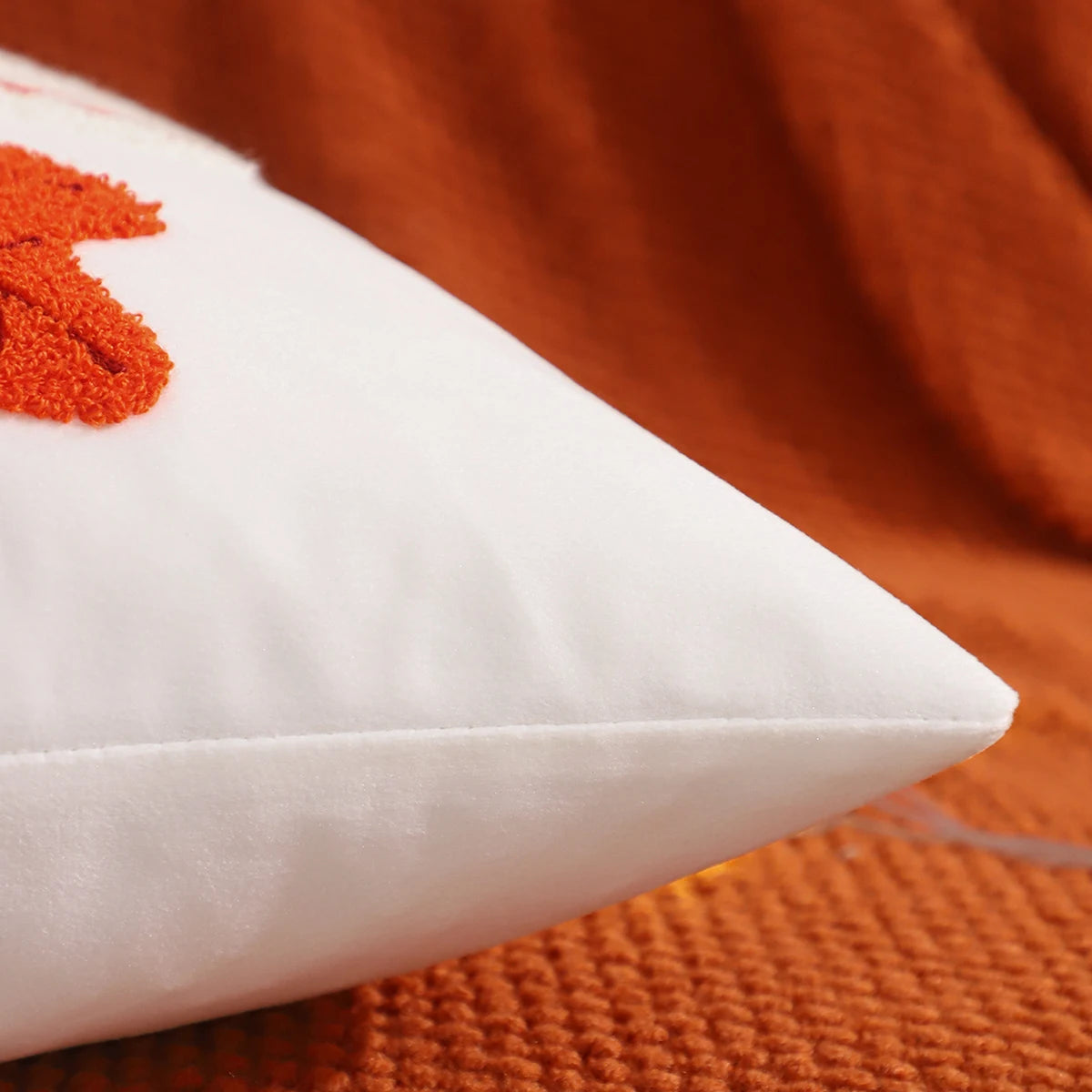 White pillow with red heart design on an orange textured surface. Velvet pillow cover with embroidered pumpkins, sunflowers, and autumn leaves – cozy fall home décor for sofa or living room.