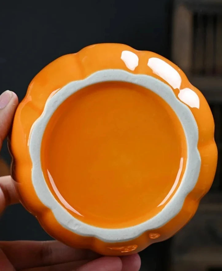 Orange ceramic dish held by a hand with a blurred background. Ceramic pumpkin candy jar with lid, decorative fall tea jar or wedding gift container for home or halloween holiday decor.