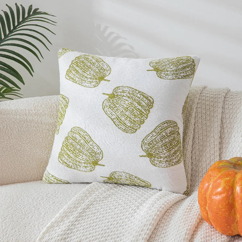 Decorative pillow with green leaf pattern on a beige couch with a pumpkin and plant in the background. Cozy fall pumpkin pillow cover for living room or bedroom