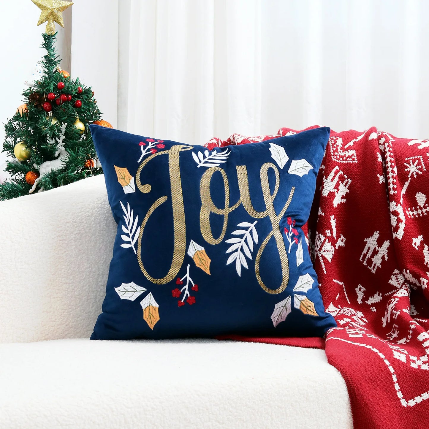 Decorative pillow with 'Joy' text on a couch with a Christmas tree in the background