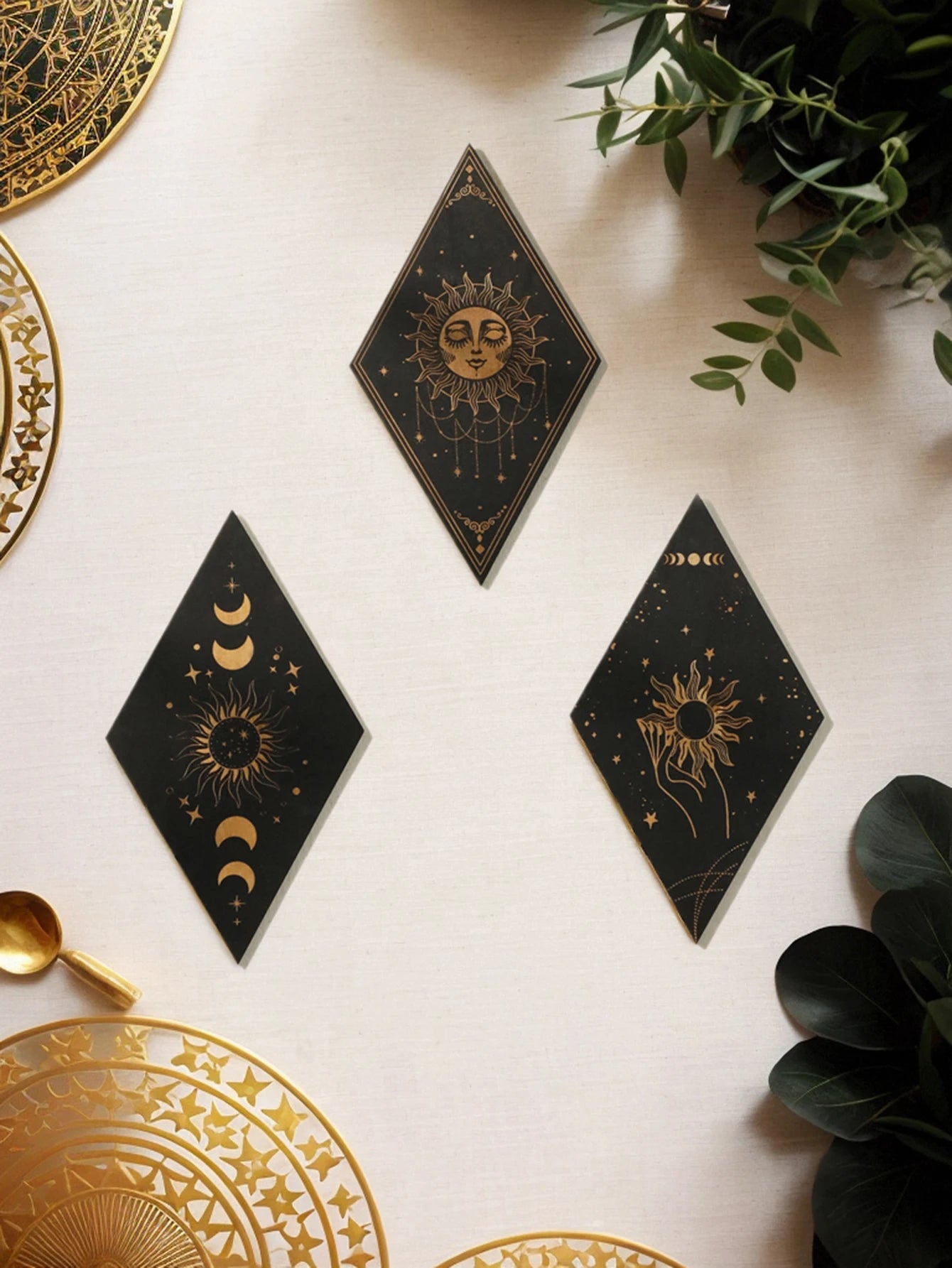 Decorative black and gold cards with celestial designs on a white surface with plants. boho home decor, wooden witchy wall hanging, moon phase wall art, gothic home decor, celestial wall pediment, snake wall hanging, sun and moon wall decor, spiritual home accents, mystical bedroom art, witchy housewarming gift