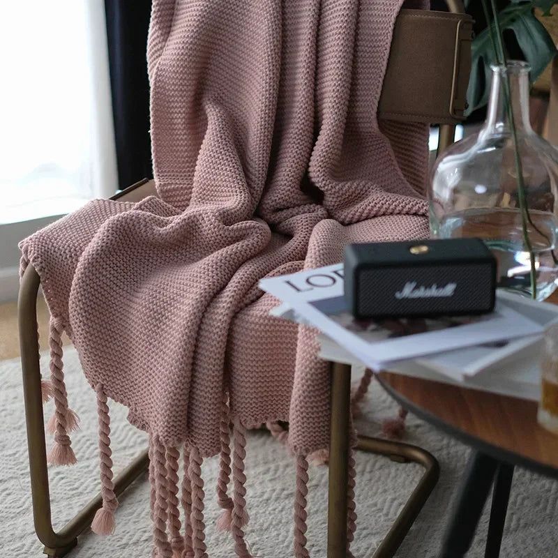 Pink knitted blanket draped over a chair with a small table holding a Marshall speaker and books in the background.