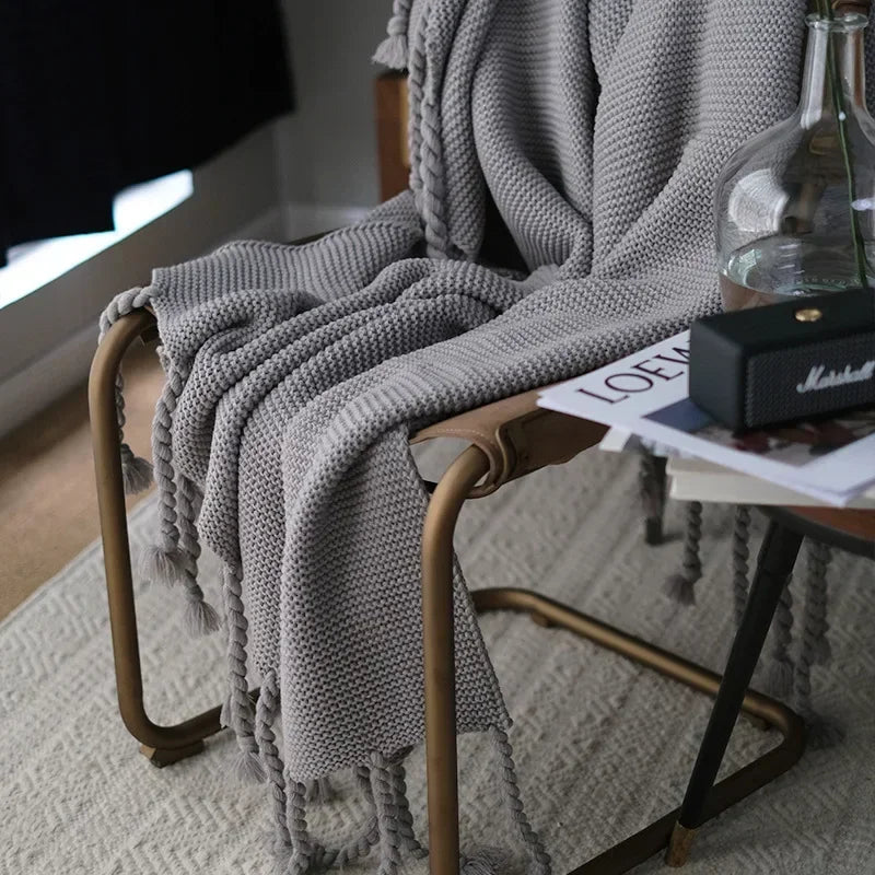Gray textured blanket draped over a chair with a small table and bottle in the background.