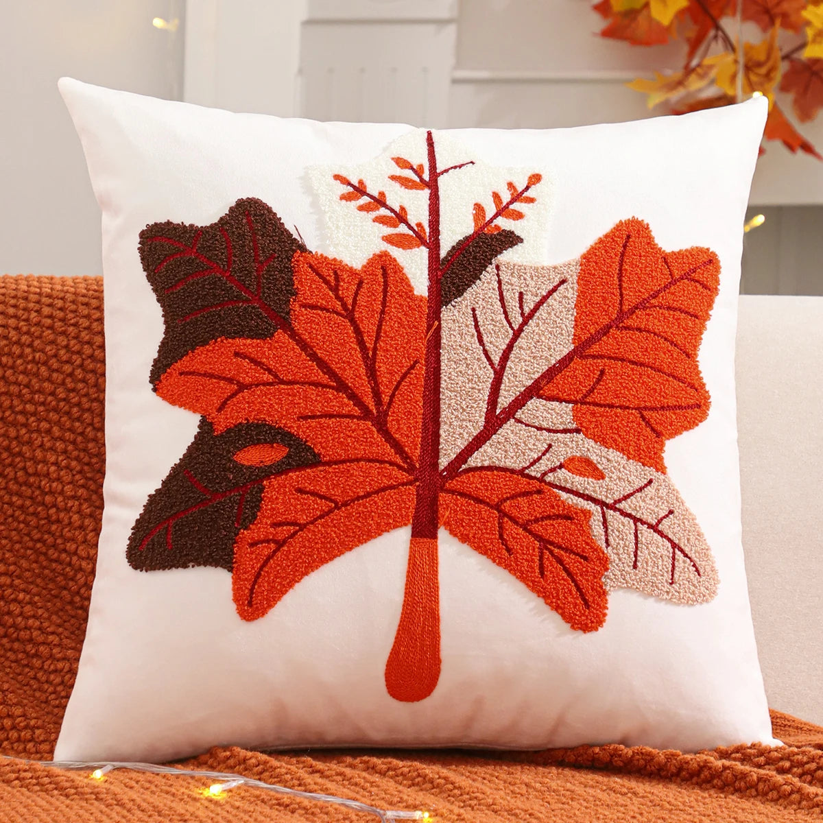 Decorative pillow with autumn leaf design on a couch. Velvet pillow cover with embroidered pumpkins, sunflowers, and autumn leaves – cozy fall home décor for sofa or living room.