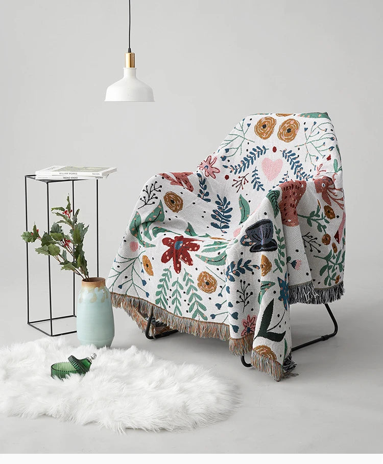 Floral-patterned blanket draped over a chair with a white background. Deer forest jacquard woven blanket with floral and woodland tapestry design – boho throw for sofa or bed, soft cotton blend decorative bedspread for cozy home décor.