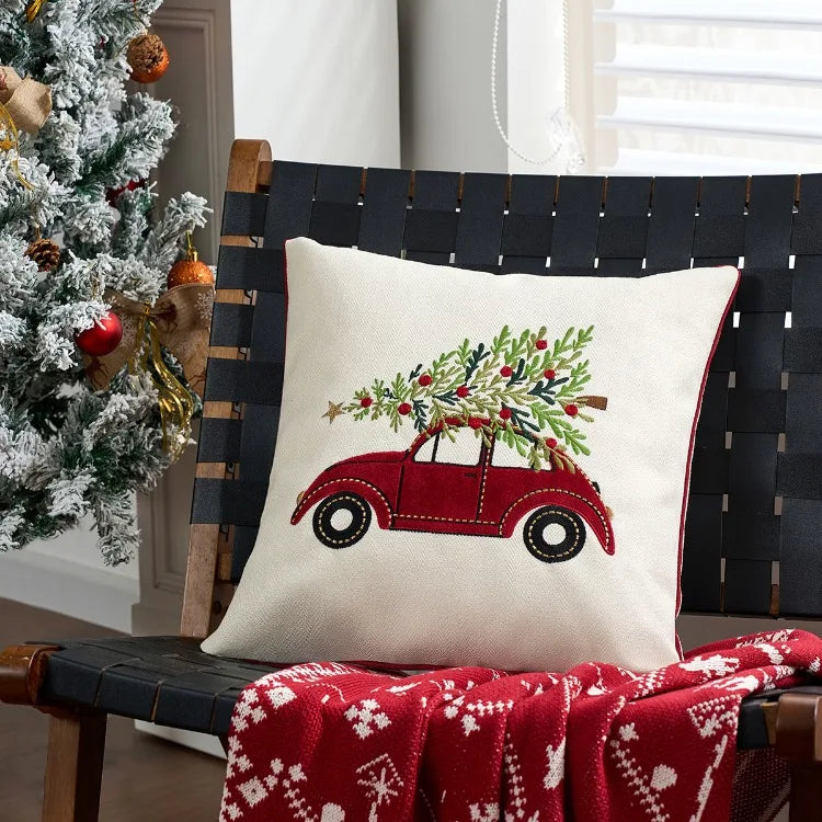 Decorative pillow with a Christmas tree and red car design on a black woven bench next to a decorated Christmas tree.