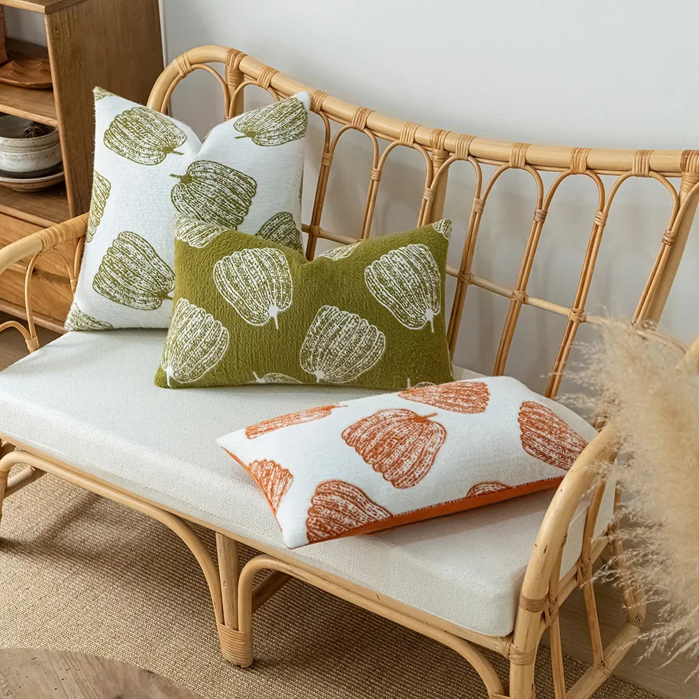 Wicker bench with patterned cushions on a neutral background. Cozy fall pumpkin pillow cover for living room or bedroom.