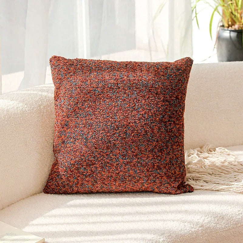 Textured red and brown pillow on a light-colored couch with a neutral background