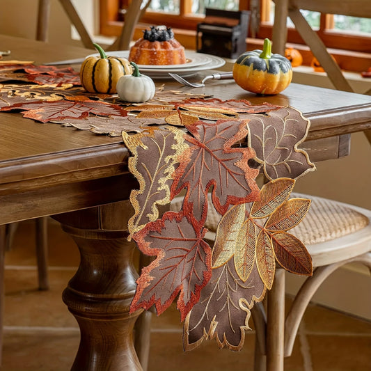 Decorative leaf-patterned table runner on a wooden table with pumpkins and fall-themed decor.