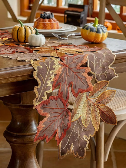 Decorative leaf-patterned table runner on a wooden table with pumpkins and a cake.