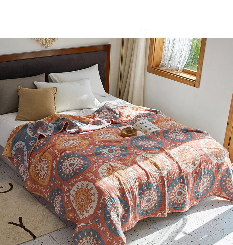Bed with a patterned comforter in a bright bedroom. Bohemian cotton gauze quilted bedspread in 4-layer muslin, breathable summer blanket for bed or sofa, lightweight soft throw in assorted colors and patterns. My Boho Home. 