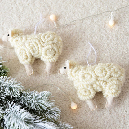 Two white knitted sheep ornaments hanging on a string with lights against a textured beige background.