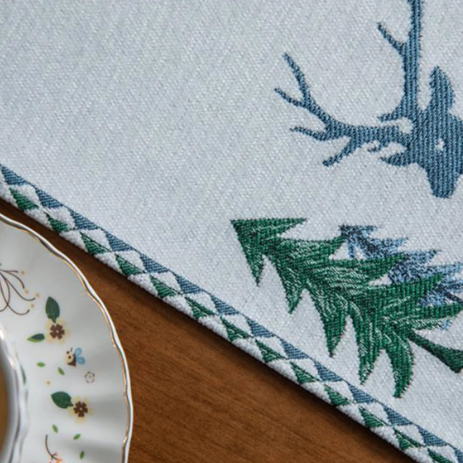 Embroidered placemat with deer and pine tree design on a wooden surface