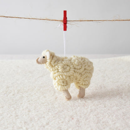 Knitted sheep ornament hanging on a clothesline with a red clip against a white background