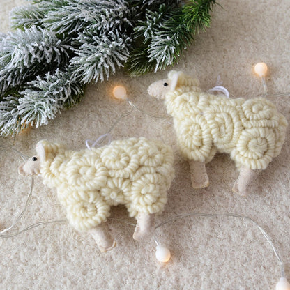 Two white knitted sheep ornaments on a textured surface with a snowy branch in the background.
