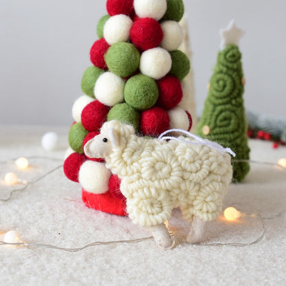 Decorative sheep and Christmas trees made of yarn on a light background with string lights.