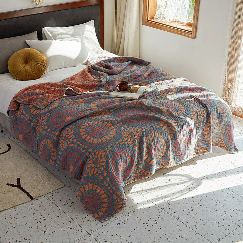 Bed with a patterned quilt in a bright bedroom. Bohemian cotton gauze quilted bedspread in 4-layer muslin, breathable summer blanket for bed or sofa, lightweight soft throw in assorted colors and patterns. My Boho Home. 
