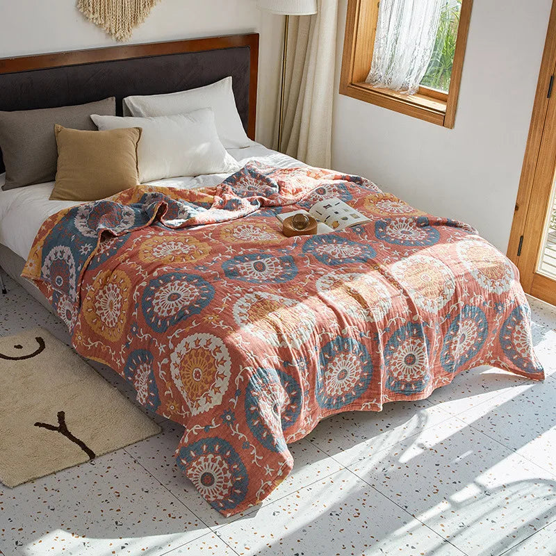 Bed with a patterned comforter in a bright bedroom. Bohemian cotton gauze quilted bedspread in 4-layer muslin, breathable summer blanket for bed or sofa, lightweight soft throw in assorted colors and patterns. My Boho Home. 