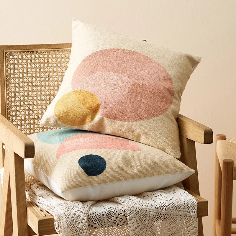 Decorative pillows with abstract patterns on a wooden chair. Colorful abstract geometric embroidered cushion cover in cotton blend, decorative pillowcase for living room, kids’ room, or boho home decor.