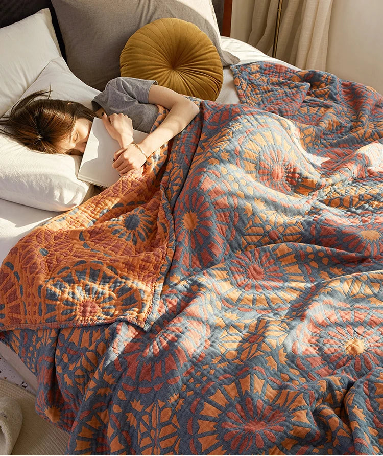 Person lying on a bed with a patterned quilt and pillows. Bohemian cotton gauze quilted bedspread in 4-layer muslin, breathable summer blanket for bed or sofa, lightweight soft throw in assorted colors and patterns. My Boho Home. 