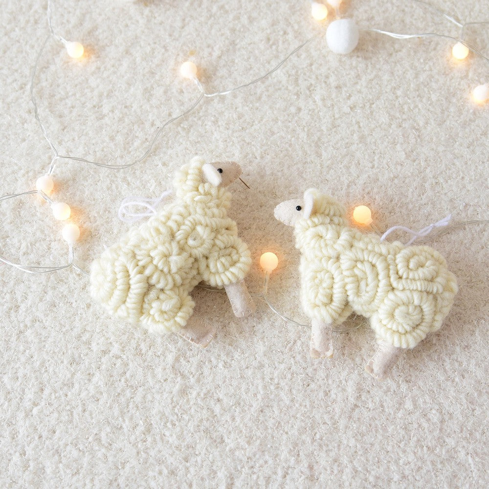 Two white sheep ornaments on a textured surface with string lights in the background.