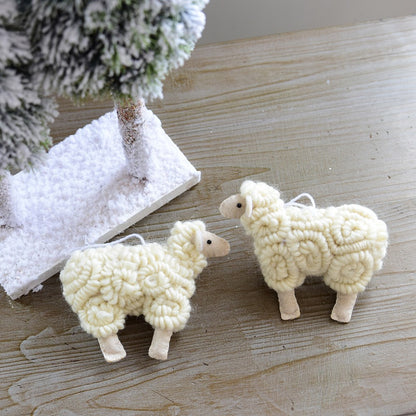Two white sheep ornaments on a wooden surface with a small tree in the background.