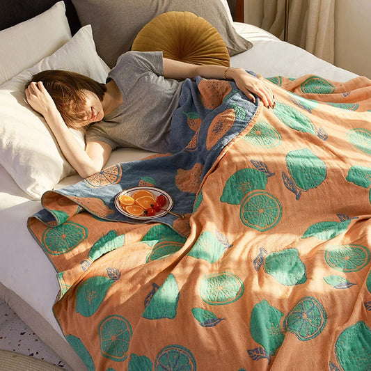 Person lying on a bed under a colorful blanket with fruit pattern. Bohemian cotton gauze quilted bedspread in 4-layer muslin, breathable summer blanket for bed or sofa, lightweight soft throw in assorted colors and patterns. My Boho Home. 