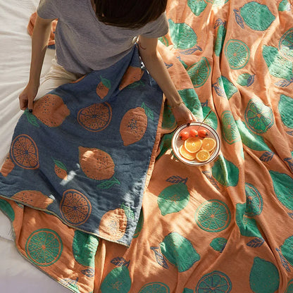 Person holding a bowl of fruit next to patterned blankets with orange and green designs. Bohemian cotton gauze quilted bedspread in 4-layer muslin, breathable summer blanket for bed or sofa, lightweight soft throw in assorted colors and patterns. My Boho Home. 