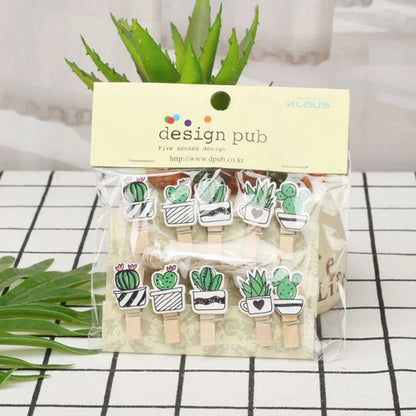 Packaged wooden clips with cactus designs on a checkered surface with plants in the background