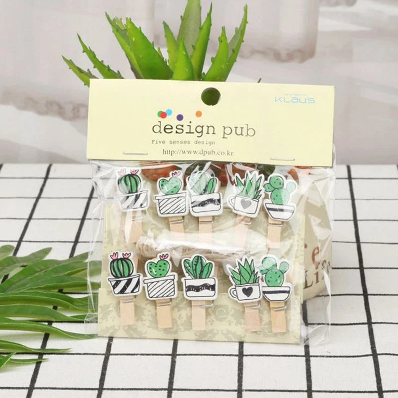 Packaged wooden clips with cactus designs on a checkered surface with plants in the background
