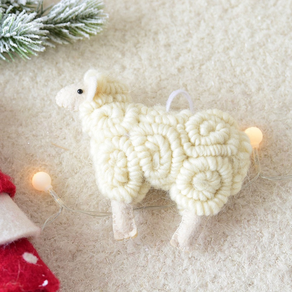White yarn sheep ornament on a textured surface with Christmas lights and decorations.