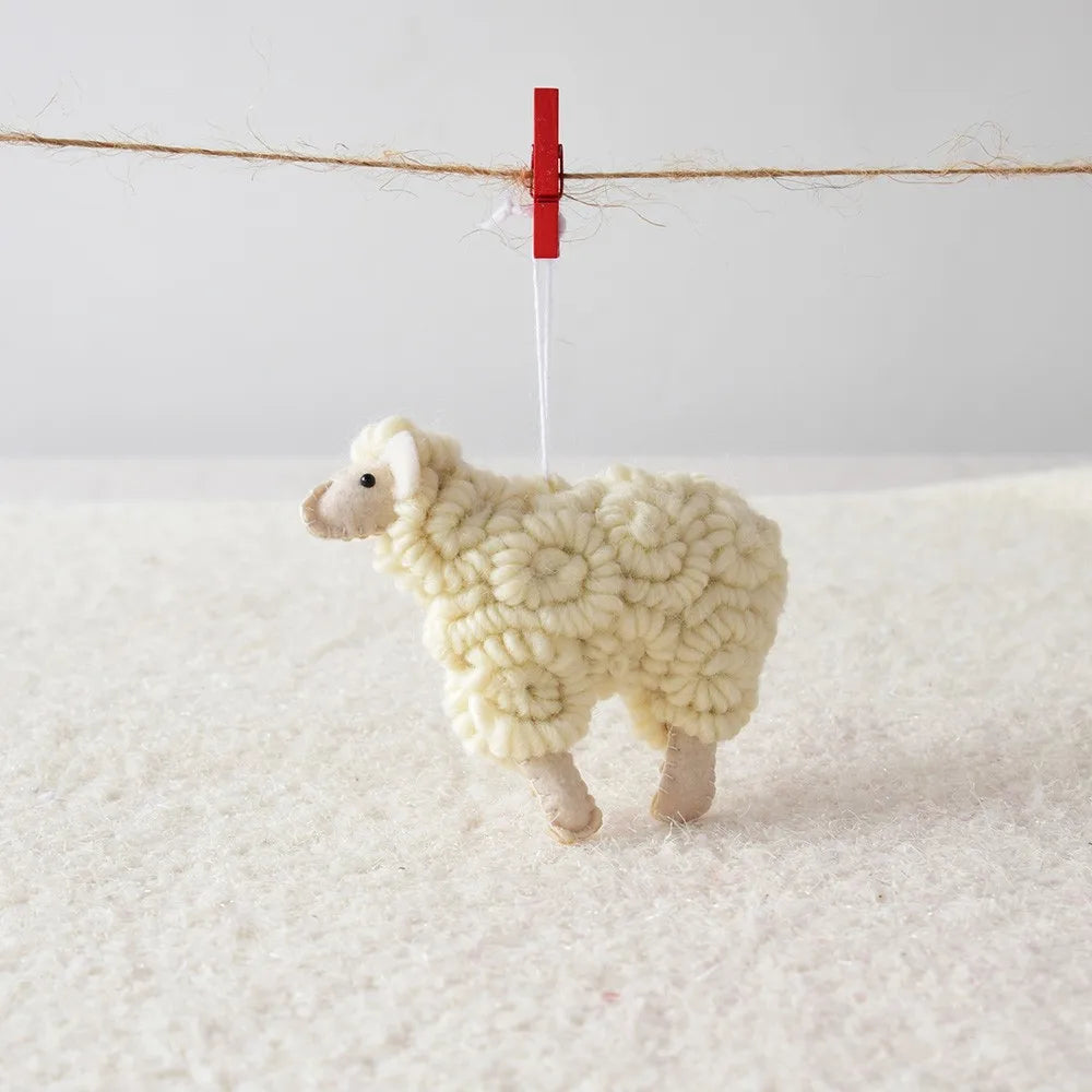 White knitted sheep Christmas ornament hanging on a red clothespin against a white background