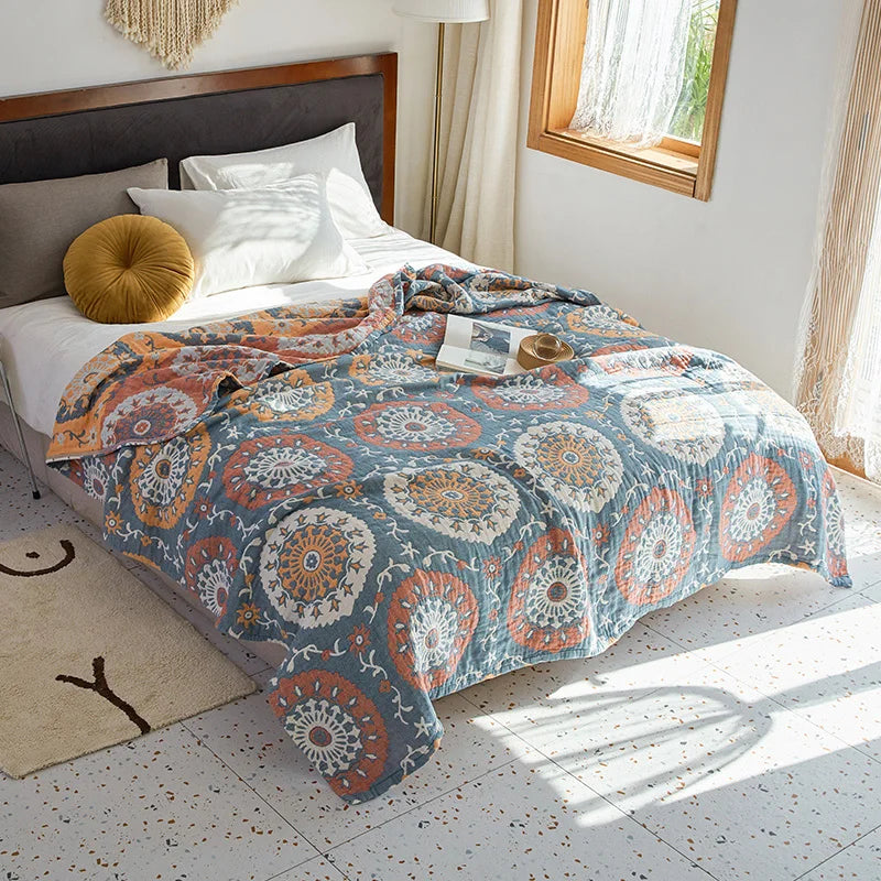 Bed with a patterned quilt in a bright bedroom. Bohemian cotton gauze quilted bedspread in 4-layer muslin, breathable summer blanket for bed or sofa, lightweight soft throw in assorted colors and patterns. My Boho Home. 