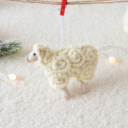 Handmade yarn sheep ornament hanging on a clothesline with a snowy background.