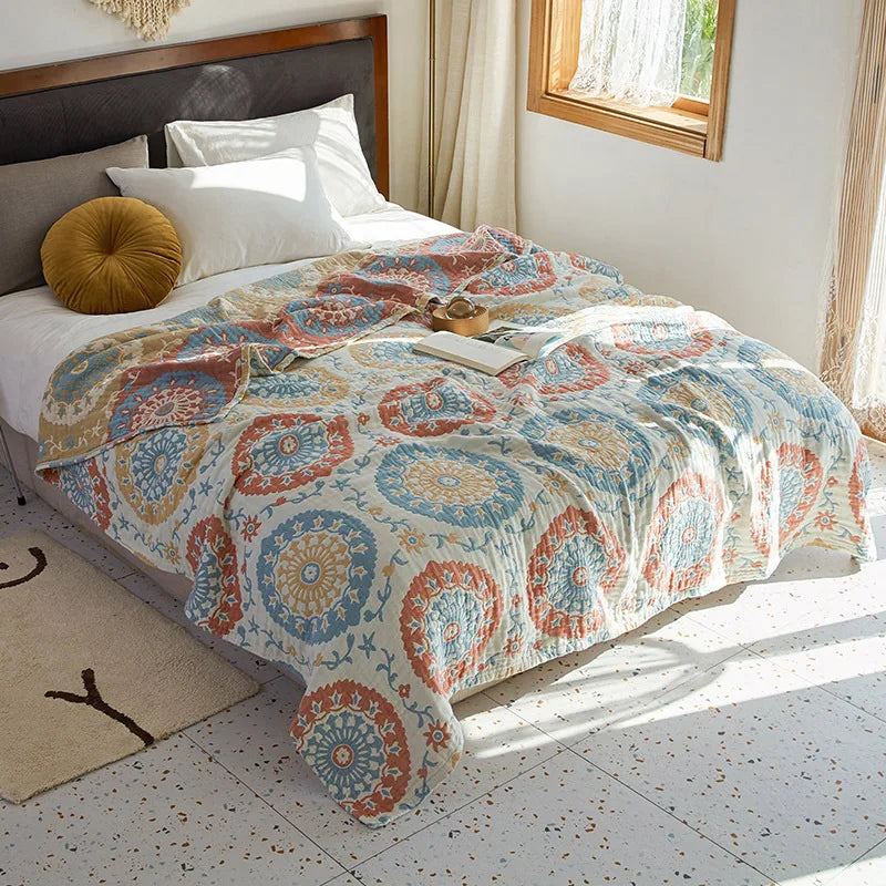 Bed with a patterned comforter in a bright bedroom. Bohemian cotton gauze quilted bedspread in 4-layer muslin, breathable summer blanket for bed or sofa, lightweight soft throw in assorted colors and patterns. My Boho Home. 