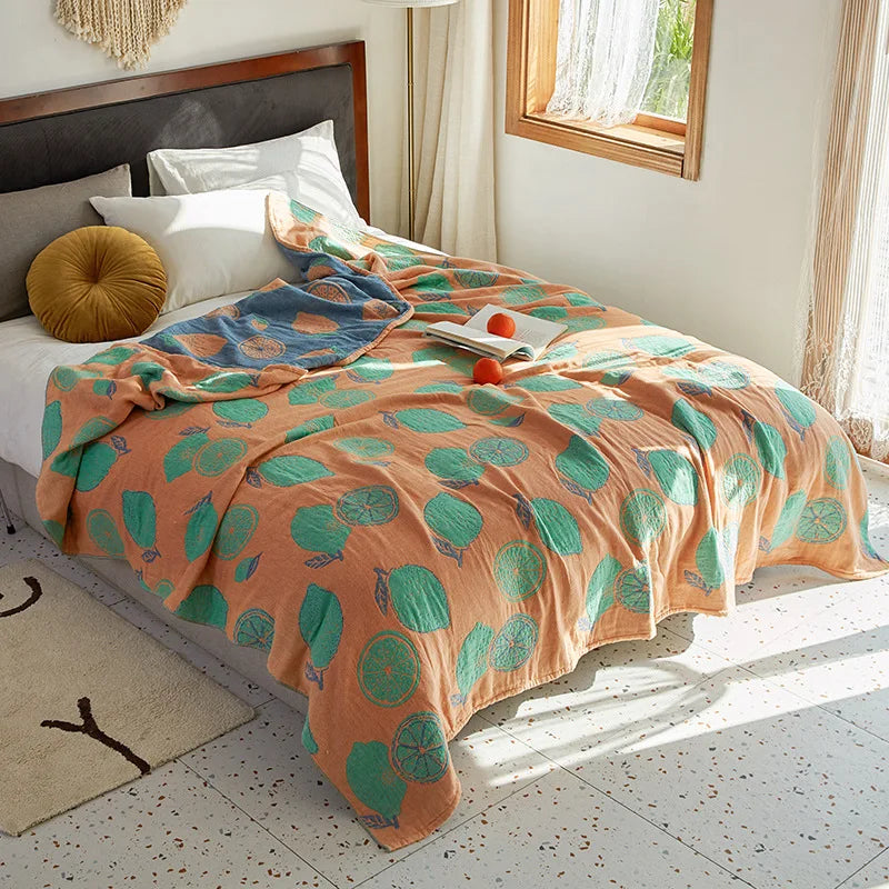 Bed with a patterned orange and green blanket in a bright bedroom. Bohemian cotton gauze quilted bedspread in 4-layer muslin, breathable summer blanket for bed or sofa, lightweight soft throw in assorted colors and patterns. My Boho Home. 
