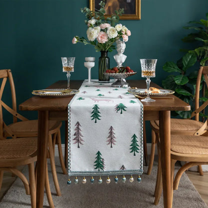 Dining table set with a decorative table runner featuring trees, glasses, and flowers against a teal wall.