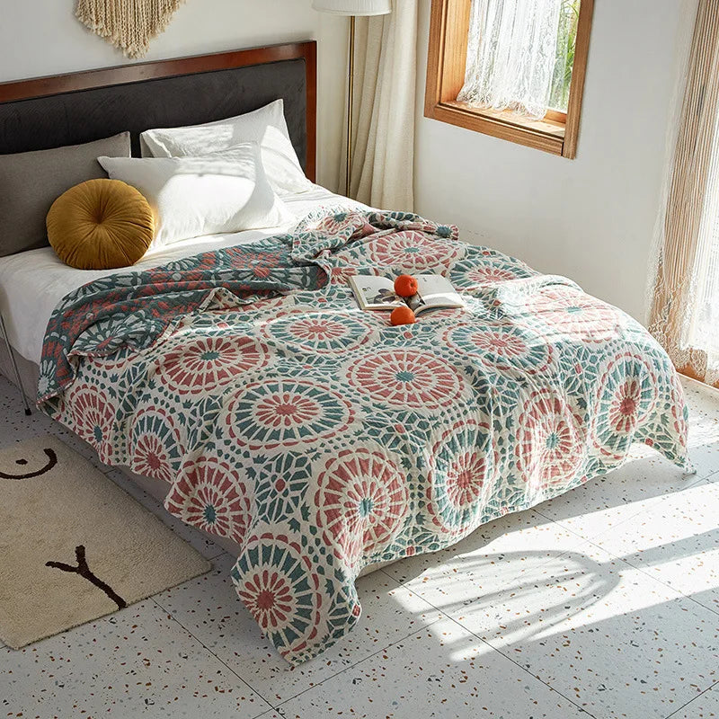 Bed with a patterned quilt in a bright bedroom. Bohemian cotton gauze quilted bedspread in 4-layer muslin, breathable summer blanket for bed or sofa, lightweight soft throw in assorted colors and patterns. My Boho Home. 