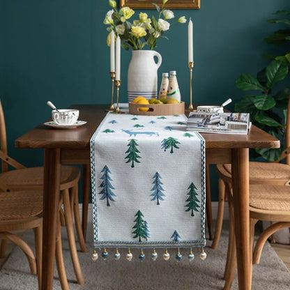 Dining table with a decorative table runner featuring tree patterns, surrounded by chairs against a teal wall.