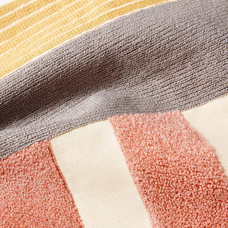Close-up of a textured fabric with geometric pattern in gray, yellow, pink, and white. Colorful abstract geometric embroidered cushion cover in cotton blend, decorative pillowcase for living room, kids’ room, or boho home decor.