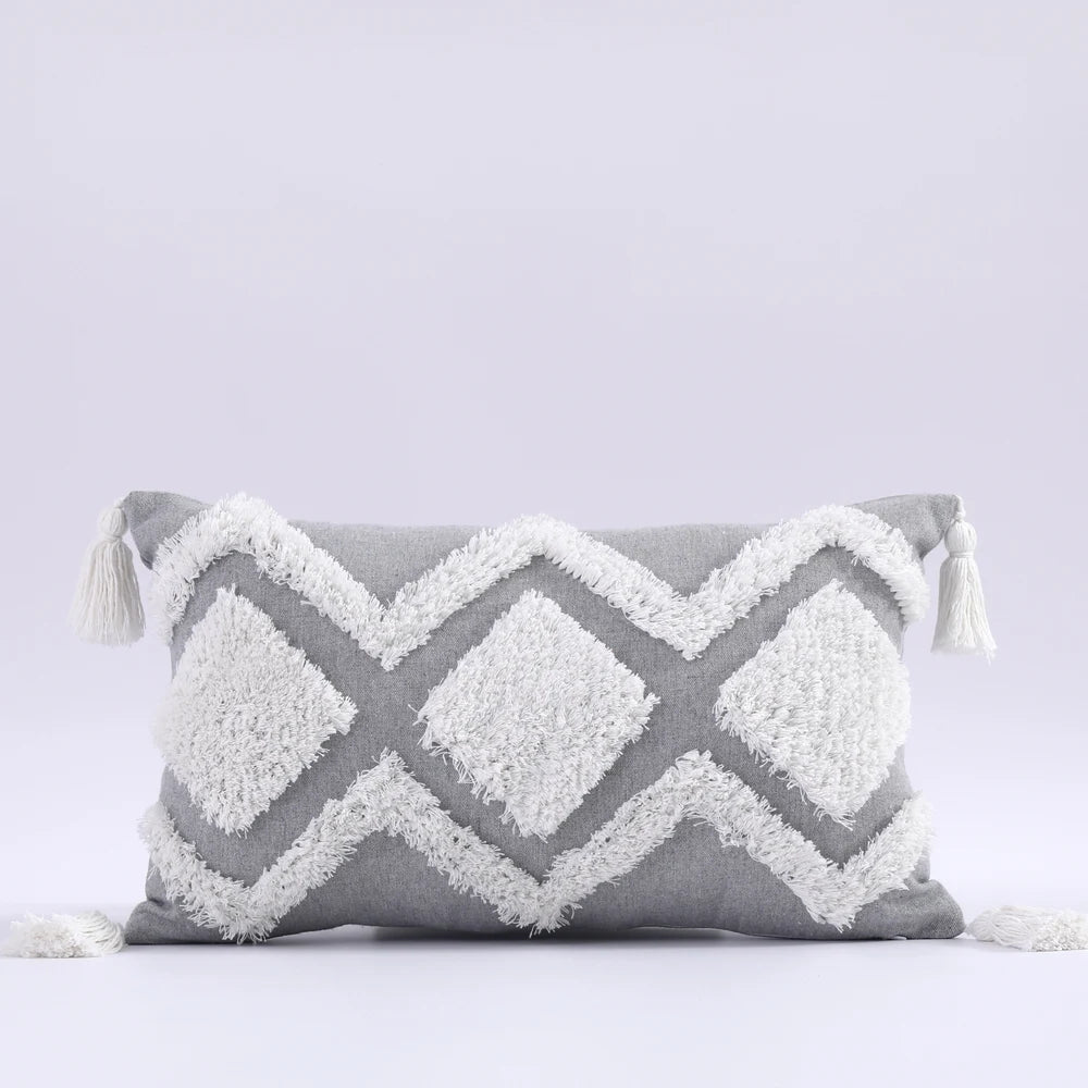 Gray and white pillow with geometric pattern and tassels on a light gray background